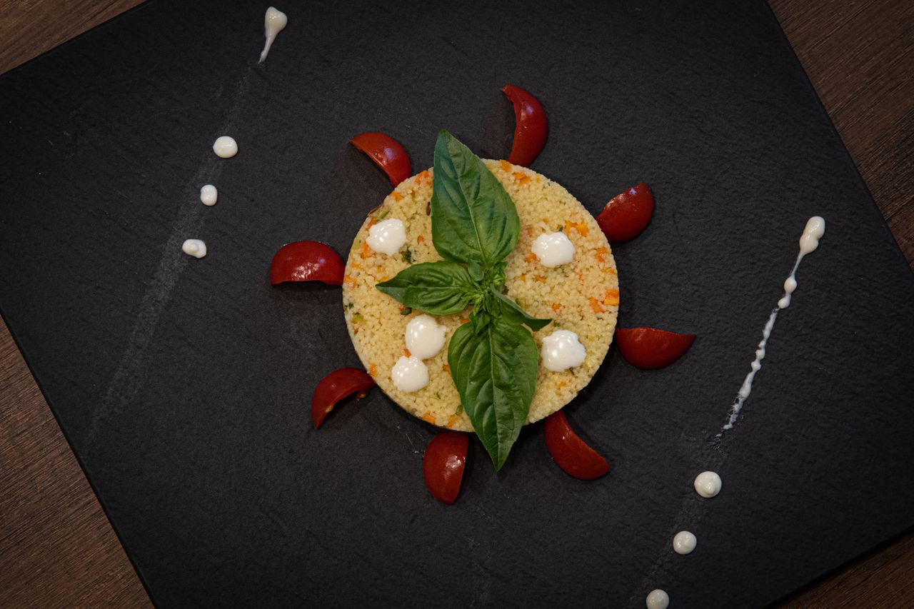 Couscous dish creatively plated with basil and cherry tomatoes on a slate plate.