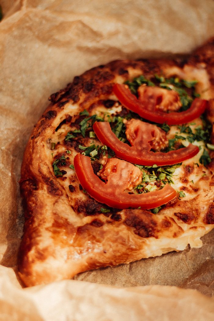 Homemade khachapuri topped with fresh tomato and herbs on parchment paper.